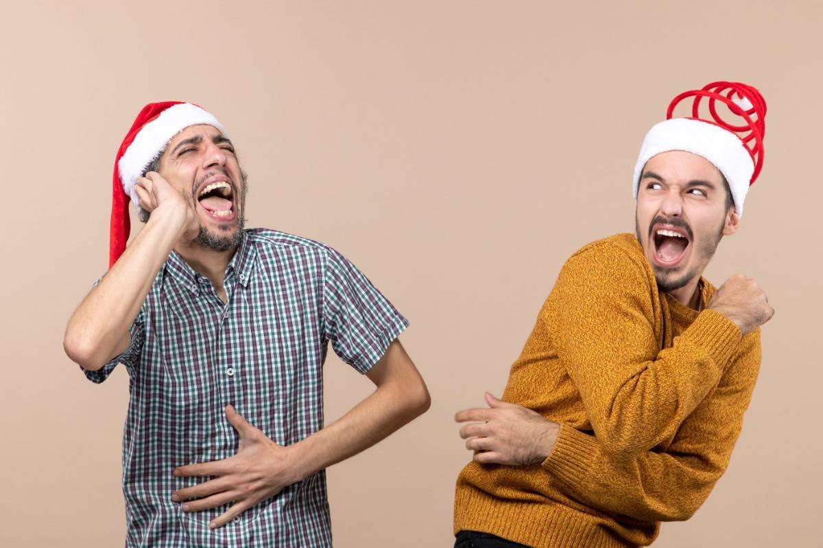 Two excited men wearing Santa hats, laughing and having fun while telling Christmas jokes. Best Christmas Jokes That’ll Get Everyone Laughing This Holiday: Two Guys in Santa Hats Having Fun.