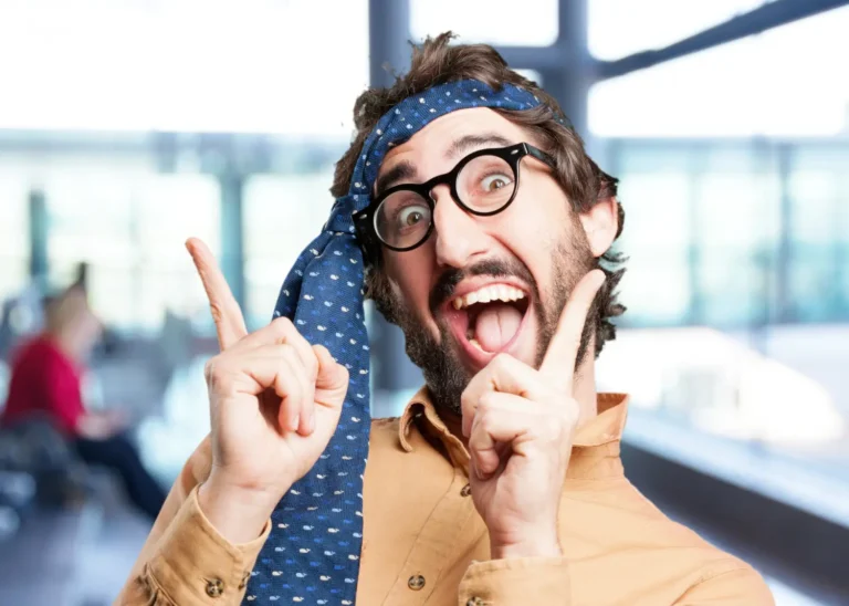 A man with glasses making a funny face and peace sign, reacting to a riddle