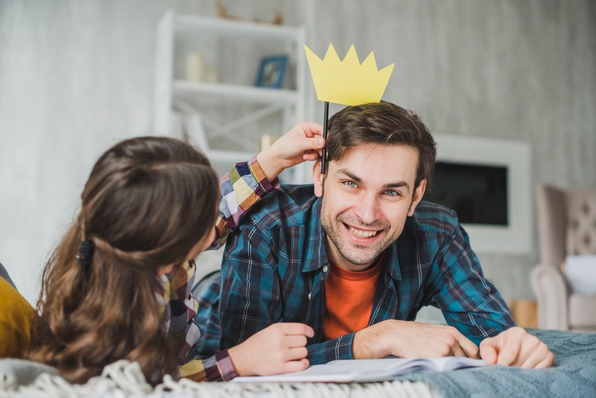Smiling dad wearing a paper crown made by his child while sharing a playful moment at home