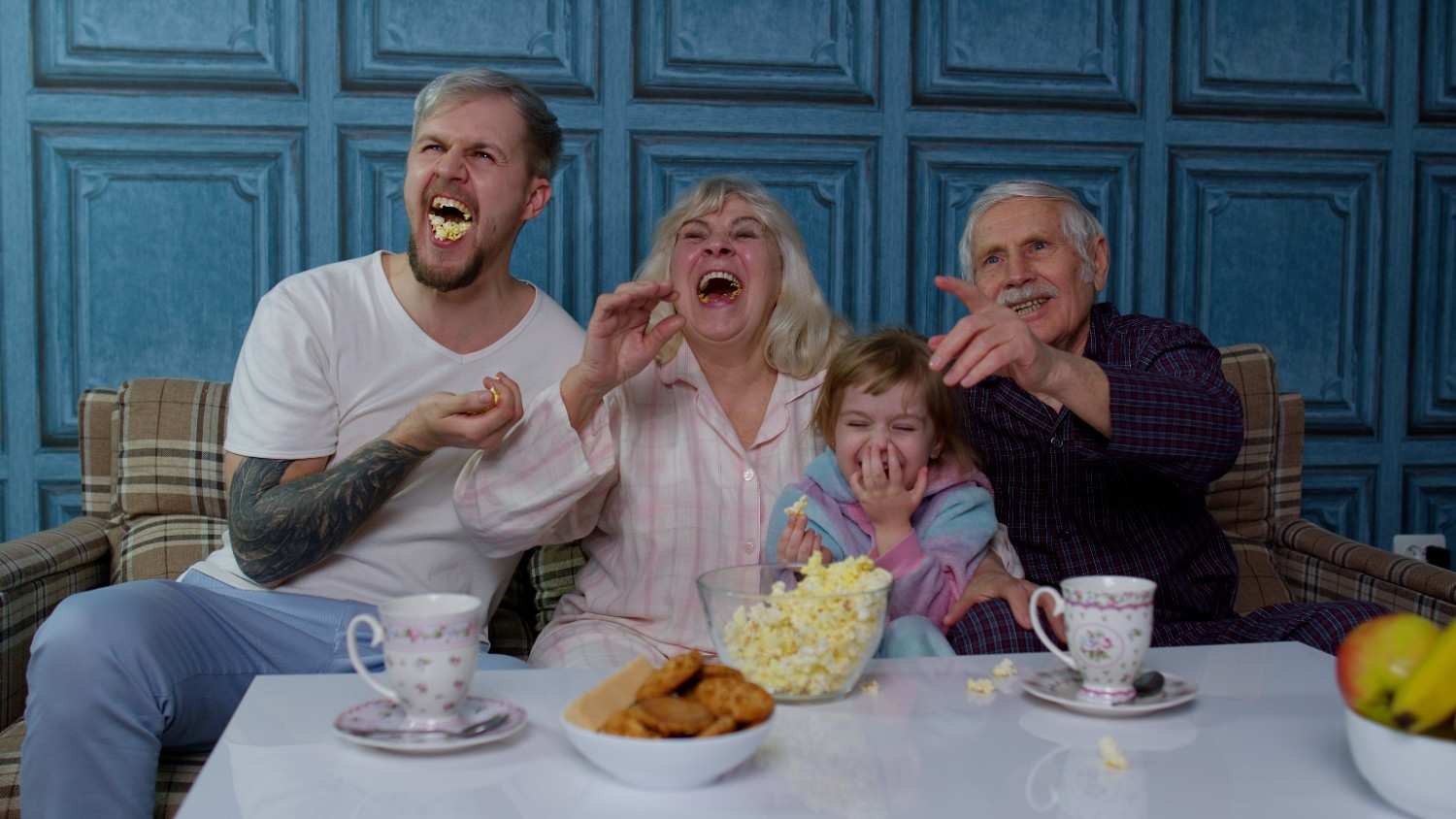 Family laughing together while eating popcorn and enjoying funny food-themed dad jokes at home.
