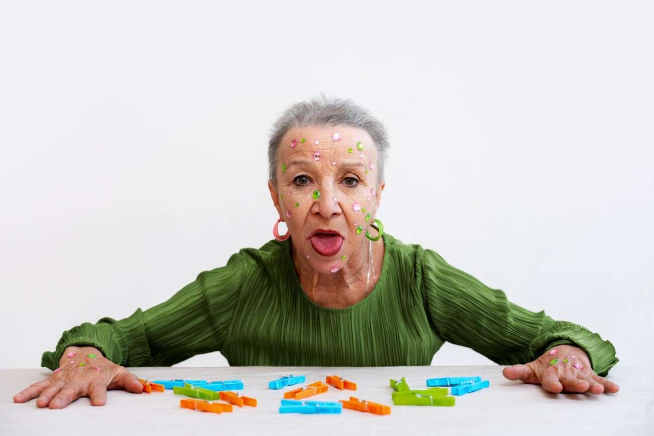 Elderly woman with colorful stickers and clothespins, reacting playfully while solving a brain teaser challenge.