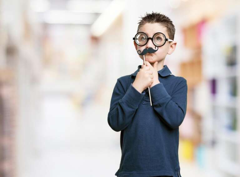 Smiling boy wearing funny glasses and fake mustache holding a stick prop.