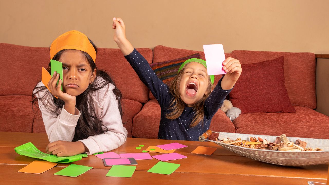 Two kids playing a colorful card game indoors, showing excitement and concentration. Fun and Easy Riddles Every Kid Will Love,