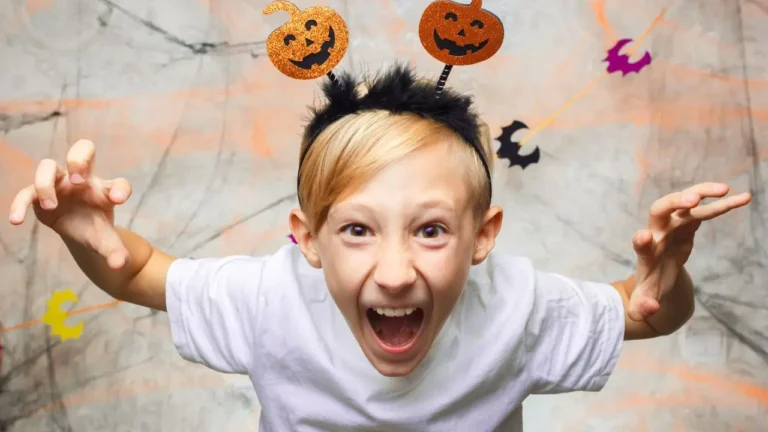 Excited child wearing pumpkin headband making a funny face during Halloween celebration.Funny Riddles for Smart Kids