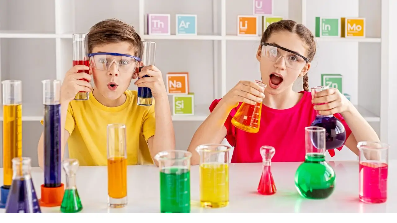Two cheerful kids wearing goggles mixing colorful liquids in lab beakers during a fun science experiment. Funny Riddles for Smart Kids That’ll Make You Giggle – Colorful Science Fun