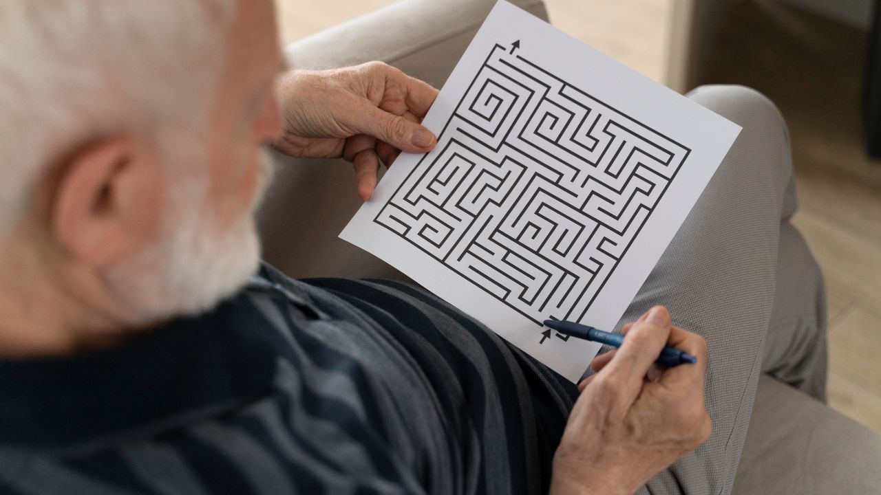An elderly man holding a printed maze puzzle and solving it with a pen, participating in the Ultimate Brain Teaser Challenge: Fun Mind Games to Try!