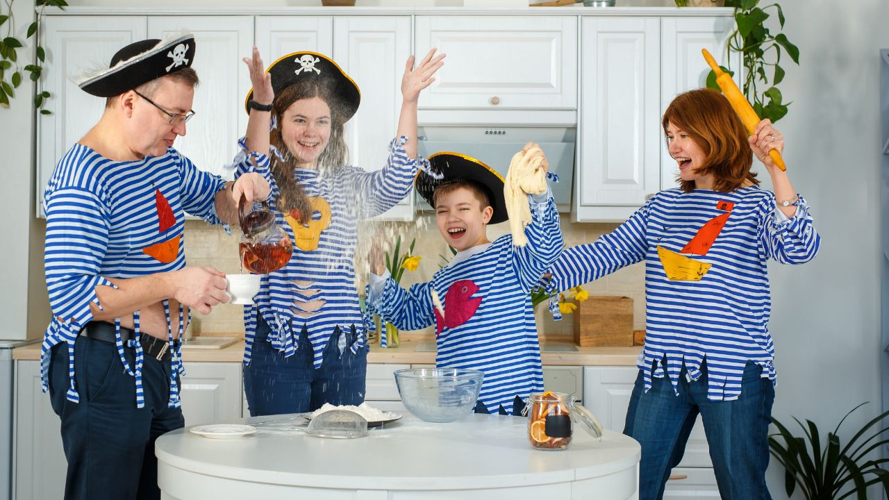 A family dressed as pirates, with playful expressions, making a mess while baking in the kitchen. Hilarious Dad Jokes That’ll Make the Whole Family Laugh