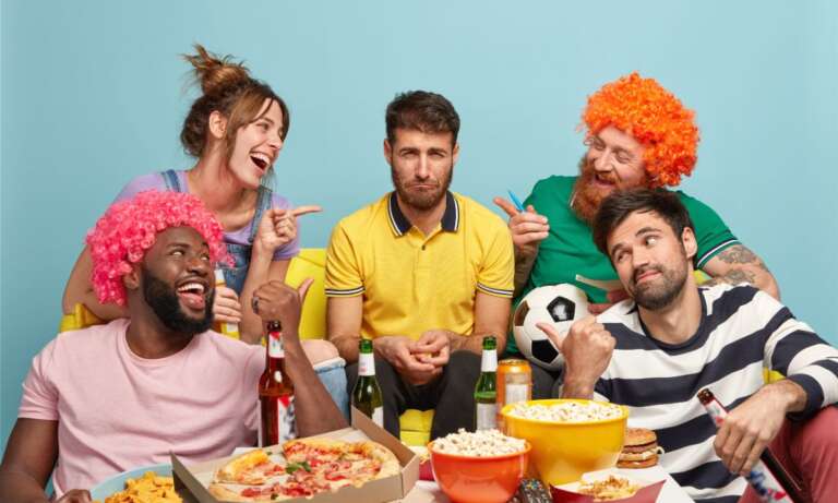Group of football fans watching match, teasing their sad friend and laughing at funny jokes for friends and family.