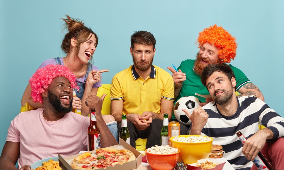 Group of football fans watching match, teasing their sad friend and laughing at funny jokes for friends and family.