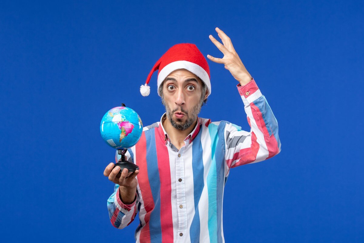 Surprised man in a Santa hat holding a globe, symbolizing world riddles and puzzles – Riddle Me Smart: Best Brain Teasers with a Twist.