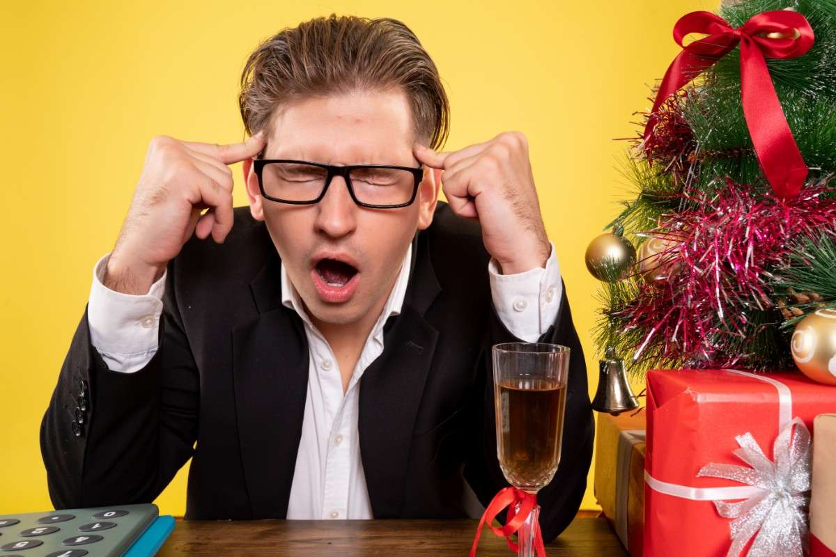 Man in a suit wearing glasses, thinking hard with a stressed expression near Christmas decorations. Brain-Tickling Funny Riddles with Answers