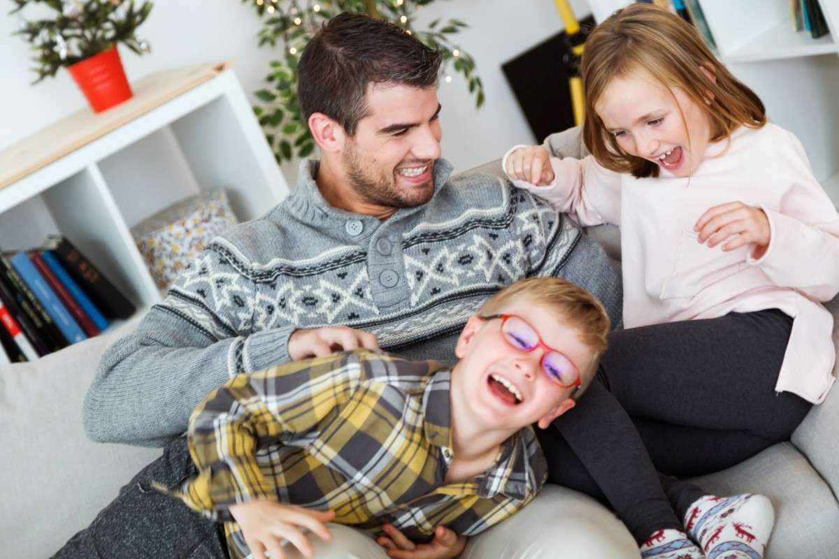 "A dad enjoying playful moments with his children on a couch, all laughing and engaging in a funny, family-friendly moment." Short & Sweet Funny Jokes for Quick Giggles.