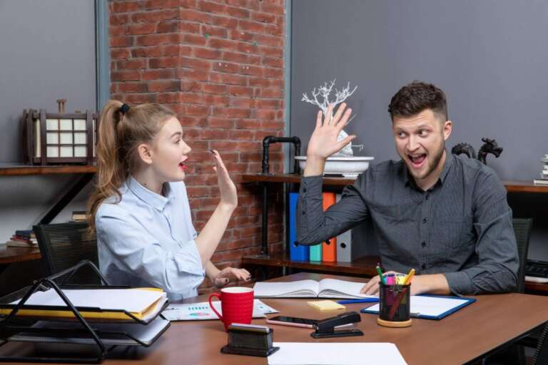 Funny work jokes moment — colleagues laughing and giving high-five in USA workplace. 50+ Funny Work Jokes for the USA Workplace