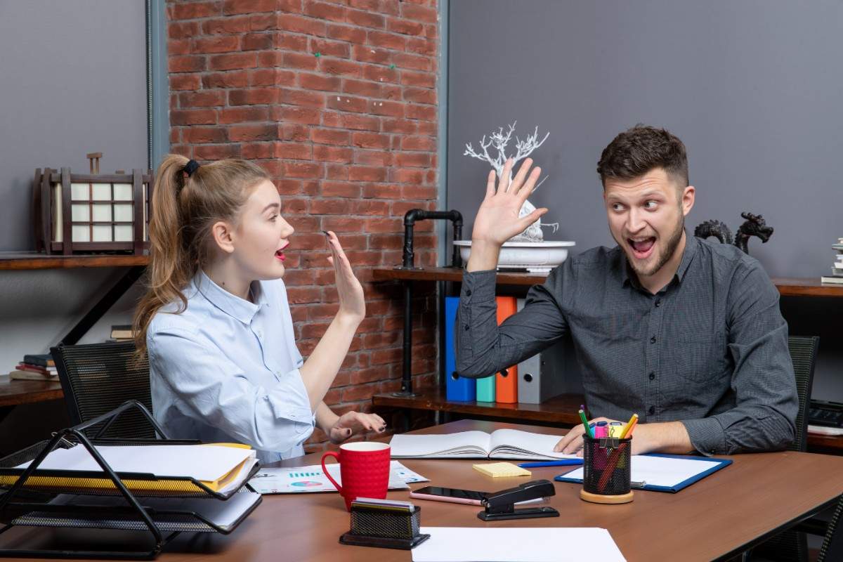 Funny work jokes moment — colleagues laughing and giving high-five in USA workplace. 50+ Funny Work Jokes for the USA Workplace