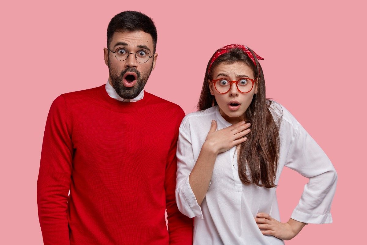Surprised man and woman reacting with shocked expressions on pink background