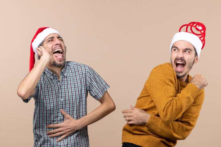 Two excited men wearing Santa hats, laughing and having fun while telling Christmas jokes. Best Christmas Jokes That’ll Get Everyone Laughing This Holiday: Two Guys in Santa Hats Having Fun.