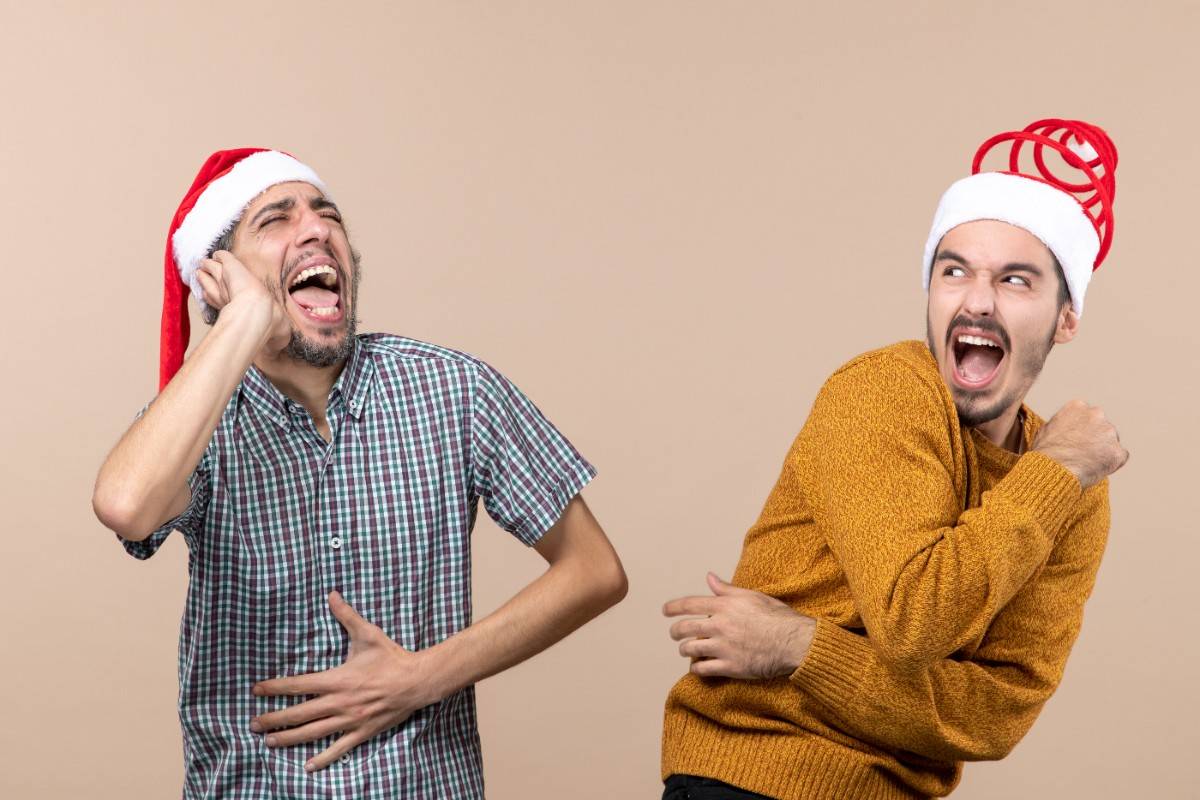 Two excited men wearing Santa hats, laughing and having fun while telling Christmas jokes. Best Christmas Jokes That’ll Get Everyone Laughing This Holiday: Two Guys in Santa Hats Having Fun.