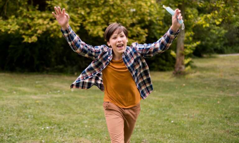 Excited boy running on grass with a big smile. Kid Jokes to Brighten Up Your Day
