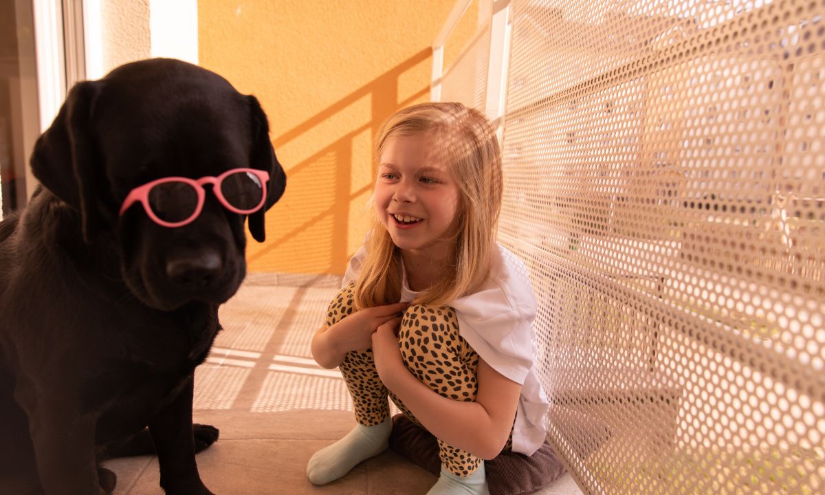 Smiling girl laughing beside a cute black dog wearing pink sunglasses