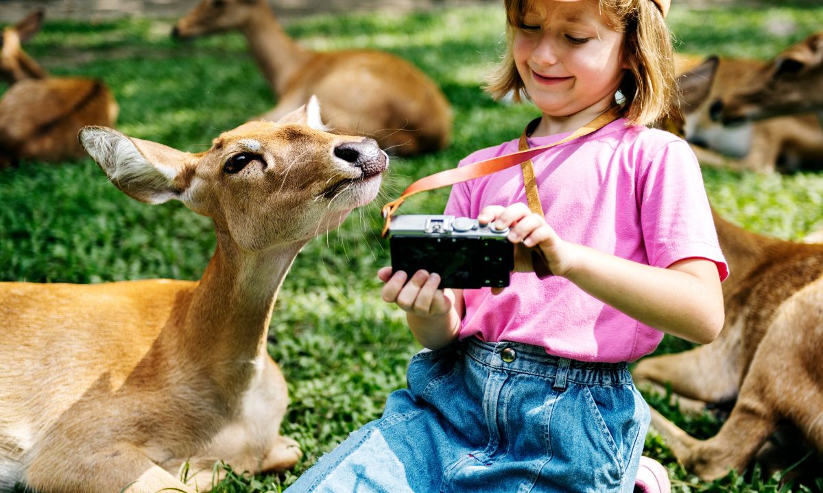 Young girl laughing with deer while holding a camera — Funny Kid Jokes playful moment
