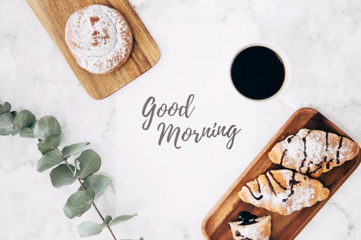 Coffee and croissants with a handwritten “Good Morning” message on a marble table,Good Morning Funny Jokes Messages to Start the Day with a Smile